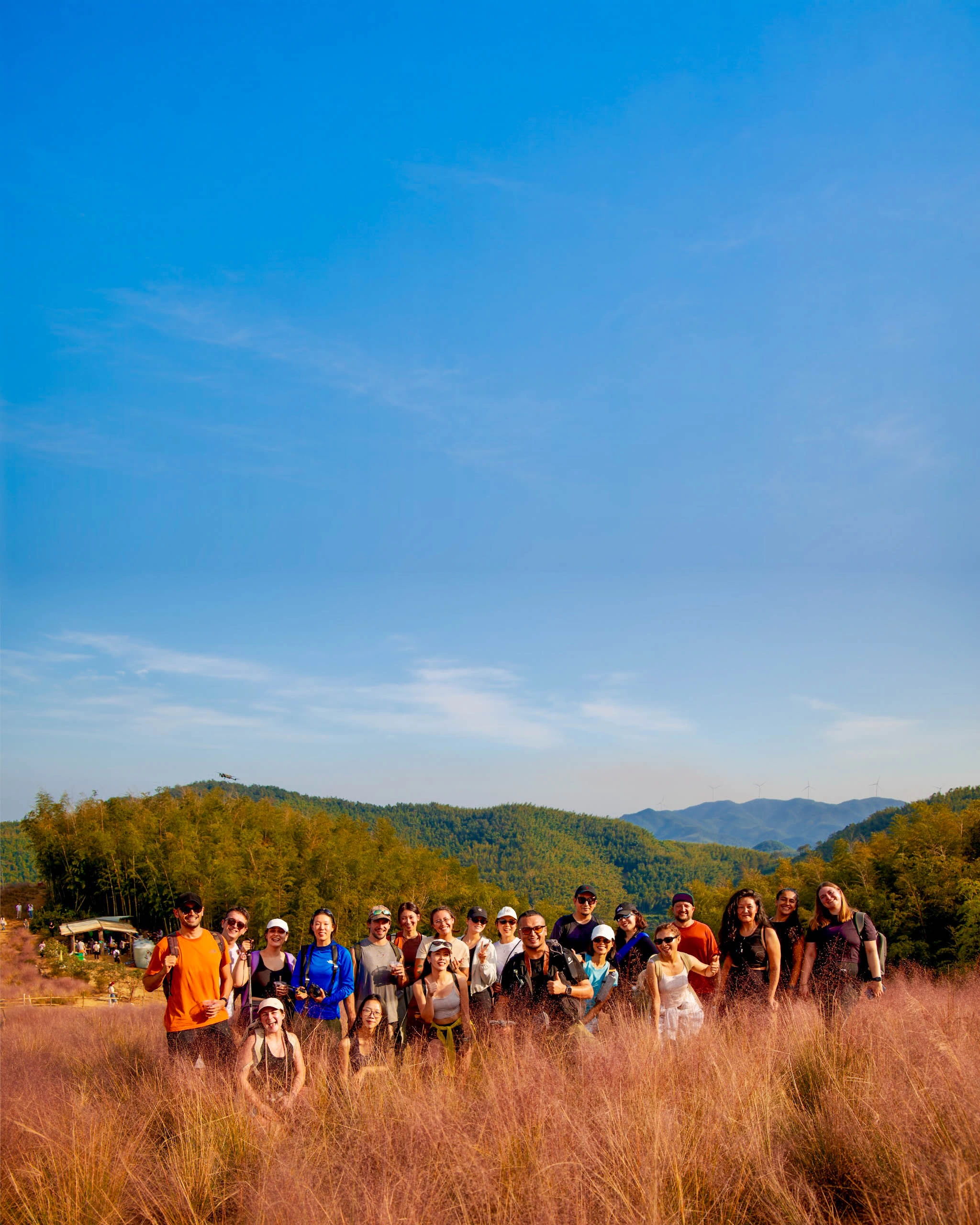 A group smiling together in golden grass, with green hills and blue sky behind them.